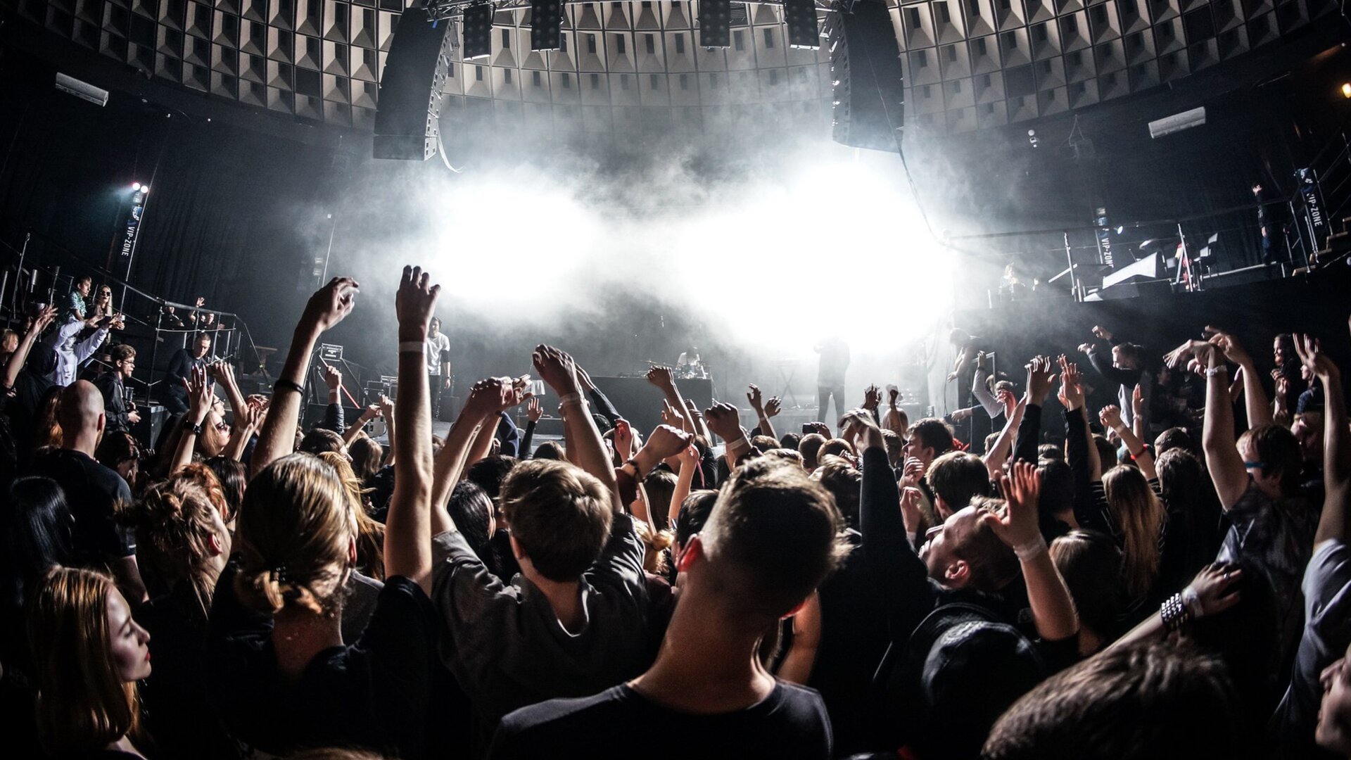 Na ekranie wyświetla się zdjęcie z koncertu. Jest zrobione z perspektywy widza. Koncert jest w budynku. Nie wiadomo, jaki zespół występuje. W tłumie znajduje się głównie młodzi ludzie, którzy mają uniesione ręce, a na nich białe opaski. Na scenie unosi się sztuczna mgła, a przez nią przebija się białe, silne światło. Sufit jest tak zaprojektowany, aby dźwięk roznosił się po całej sali. Służą do tego specjalne wyżłobienia oraz duże głośniki, które są lekko wygięte w kształcie łuku.