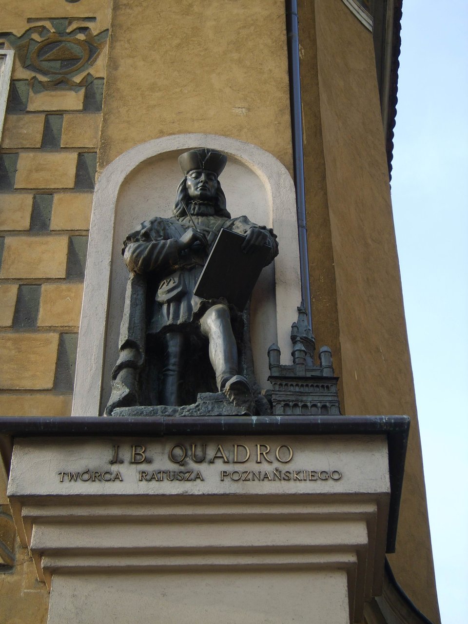 Rzeźba Jana Baptysty Quadro (Giovanni Battista di Quadro). Rzeźba powstała w XX w. na kamienicy w Poznaniu, w której mieszkał budowniczy. Quadro pochodził z okolic jeziora Como, na pograniczu włosko-szwajcarskim. Z tych okolic pochodziło wielu budowniczych pracujących w Europie Środkowej – w Niemczech, Czechach, na Śląsku w Polsce. Zwano tych architektów „komaskami” (od nazwy jeziora Como). Rzeźba Jana Baptysty Quadro (Giovanni Battista di Quadro). Rzeźba powstała w XX w. na kamienicy w Poznaniu, w której mieszkał budowniczy. Quadro pochodził z okolic jeziora Como, na pograniczu włosko-szwajcarskim. Z tych okolic pochodziło wielu budowniczych pracujących w Europie Środkowej – w Niemczech, Czechach, na Śląsku w Polsce. Zwano tych architektów „komaskami” (od nazwy jeziora Como). Źródło: domena publiczna.