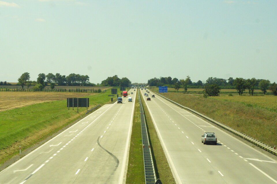 Na zdjęciu autostrada, dwa pasy i pobocze w każdym kierunku. Po obu stronach pola uprawne.