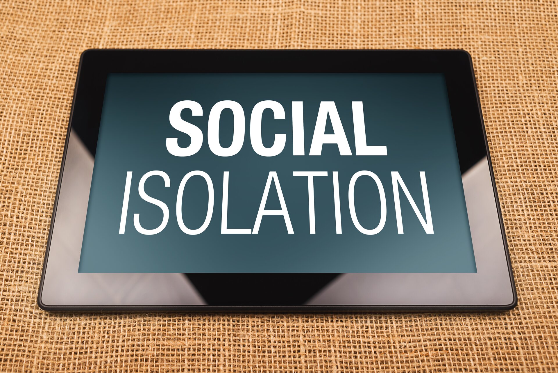 Ilustracja przedstawia cyfrowe wykluczenie. Ukazuje ona tablet z napisem na wyświetlaczu SOCIAL ISOLATION.