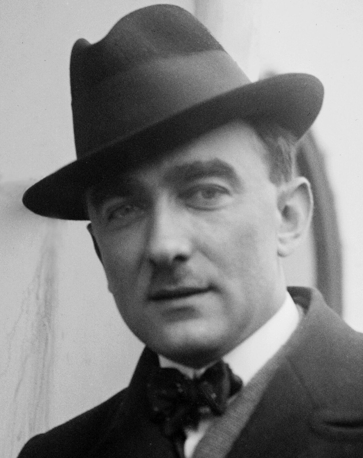 Ilustracja przedstawia fotografię Karola Szymanowskiego, polskiego pianistę i kompozytora. Mężczyzna ukazany jest od ramion w górę oraz w pozycji frontalnej (en face). Wirtuoz ma na sobie płaszcz i białą koszulę z przepasaną muszką pod szyją. Postać wyróżnia wąs i okrągły kapelusz.