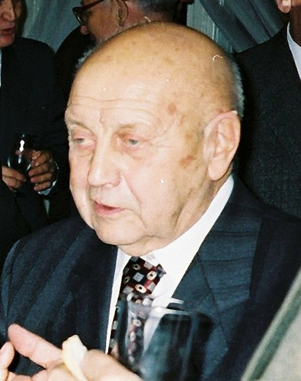 Na zdjęciu popiersie starszego mężczyzna z dużą łysiną. Ubrany w garnitut i krawat.