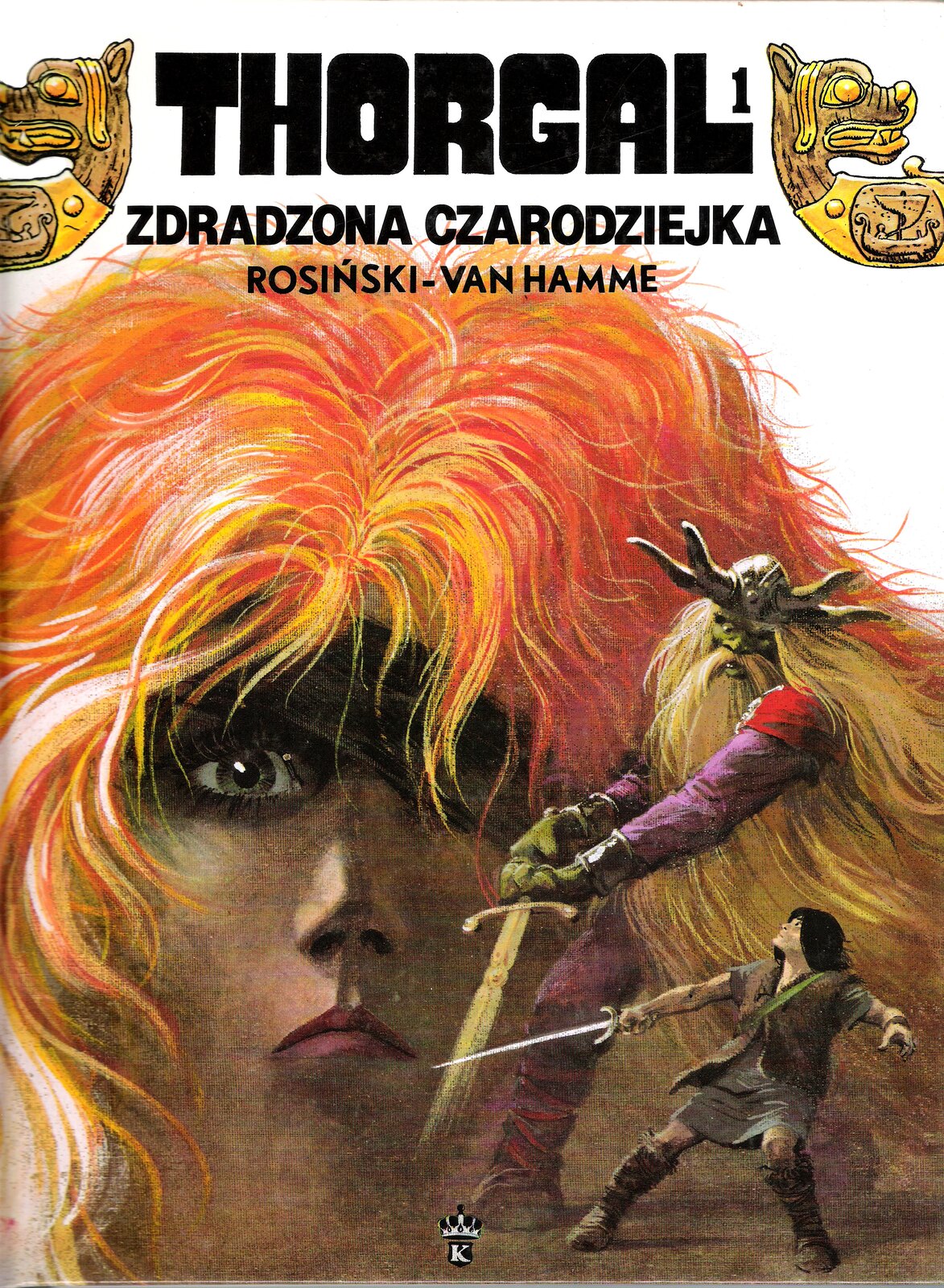 Ilustracja przedstawia okładkę komiksu Jeana Vana Hamme'a „Thorgal. Zdradzona czarodziejka”, zaprojektowaną przez Grzegorza Rosińskiego. Okładka przedstawia twarz rudowłosej dziewczyny i dwie mniejsze, walczące z sobą na miecze postacie. U dołu znajduje się czarnowłosy wojownik z mieczem w prawej dłoni. Głowę ma podniesioną na większego od siebie wikinga o zielonej twarzy i ubranego w hełm z rogami. Wiking trzyma swój miecz oburącz. Ma długie włosy i brodę do pasa. Groźnym wzrokiem spogląda na przeciwnika. W górnej części okładki znajduje się tytuł i nazwisko autora. Po bokach napisy dekorowane są głowami smoków.