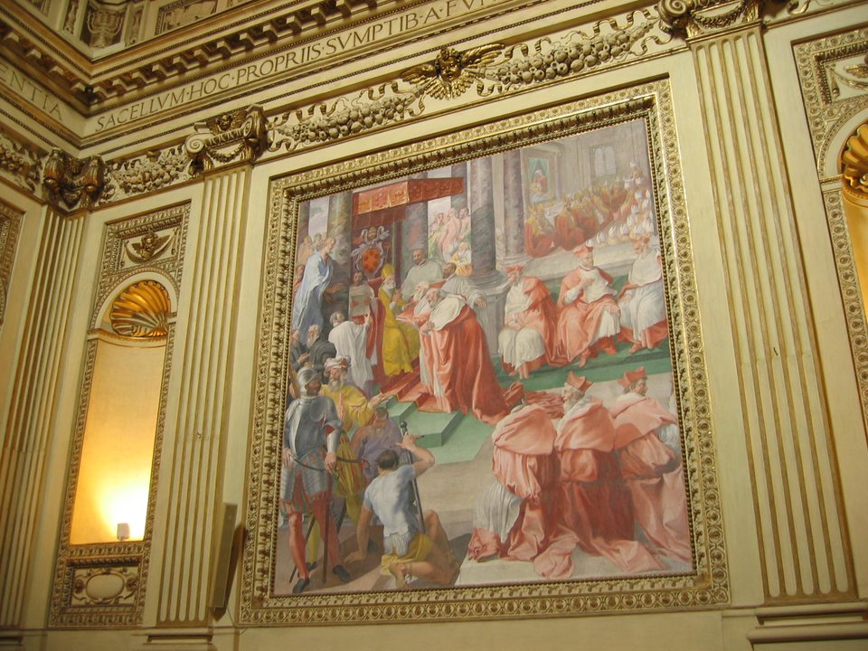 Pius IV (1559-1565) – fresk w kaplicy kościoła Rzymskiego przedstawiający Piusa IV, który wydaje bullę „Benedictus Deus”, potwierdzającą dekrety soboru trydenckiego Pius IV (1559-1565) zaraz po wyborze odciął się od działań swojego poprzednika, zapowiedział reformy w Kościele. Zaczął od pozbycia się nepotów poprzednika Pawła IV Carafy, a na najbliższego doradcę wyznaczył znanego z pobożności i religijności późniejszego świętego Karola Boromeusza (swojego siostrzeńca, a zatem to także był nepotyzm). Najważniejsze było jednak wznowienie zawieszonych obrad soboru trydenckiego i doprowadzenie jego obrad do szczęśliwego końca. Ostatnie sesje odbyły się 3 i 4 grudnia 1563 r., a 26 stycznia 1564 r. papież zatwierdził dokumenty, w tym wyznanie wiary. W tym samym 1564 r. ogłoszono nowy „Indeks Ksiąg Zakazanych”. Papież zreformował też procedury wewnętrzne Kurii – m.in. dotyczące konklawe. Prezentowany fresk (1588) autorstwa Pasquale Cati znajduje się w kaplicy Altempsów w bazylice Najświętszej Marii Panny na Zatybrzu w Rzymie. Źródło: Torvindus, Pius IV (1559-1565) – fresk w kaplicy kościoła Rzymskiego przedstawiający Piusa IV, który wydaje bullę „Benedictus Deus”, potwierdzającą dekrety soboru trydenckiego, 2004, fresk, licencja: CC BY-SA 3.0.