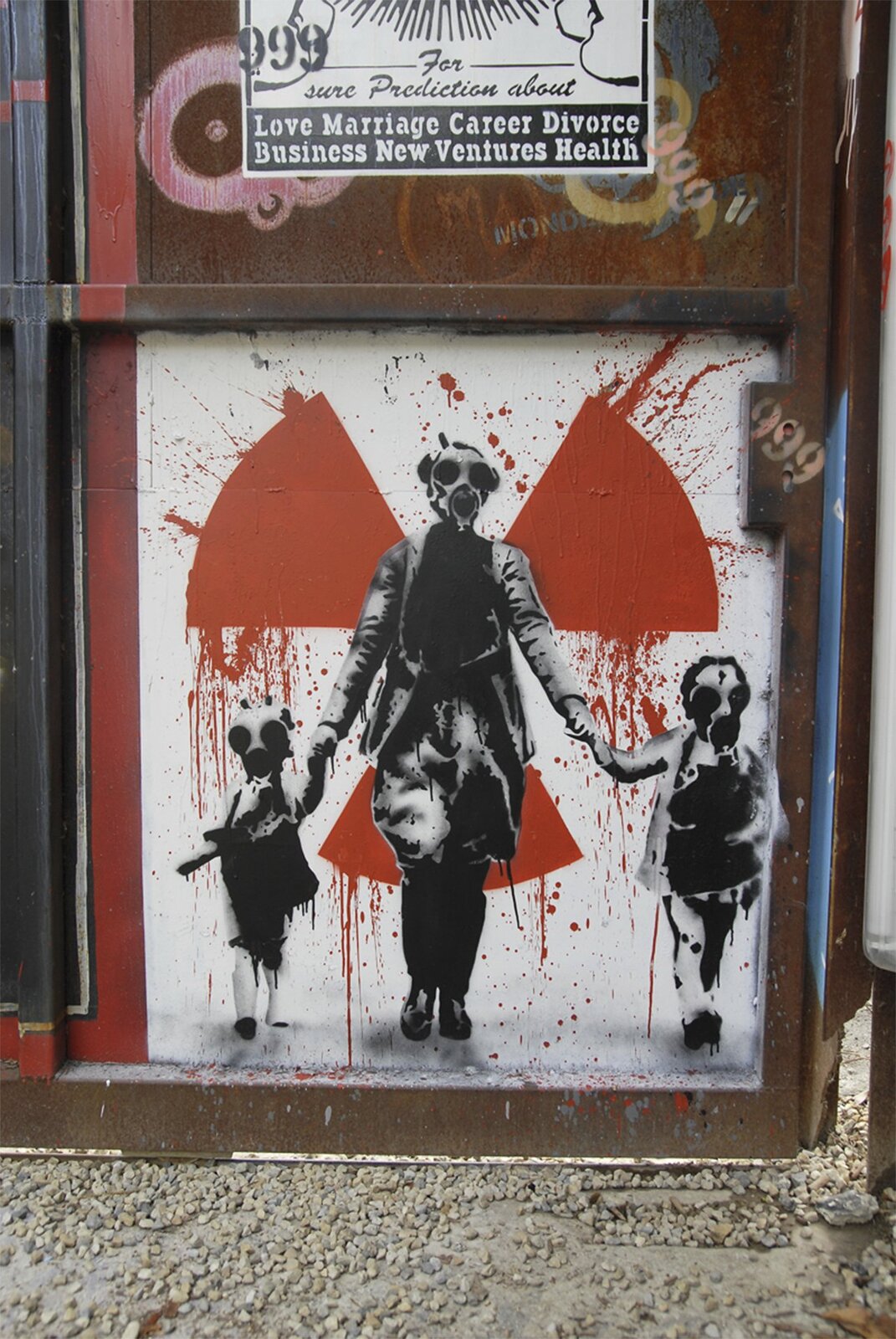 Zdjęcie przedstawia krytyczne w stosunku do energetyki atomowej graffiti na stalowym kontenerze. Na białym tle namalowany jest czerwoną farbą wiatraczek, symbol ostrzegawczy przed promieniowaniem radioaktywnym. Na tle tego znaku znajdują się czarnobiałe postacie kobiety z dwójką dzieci trzymanych za ręce. Cała trójka ma na twarzach maski przeciwgazowe.