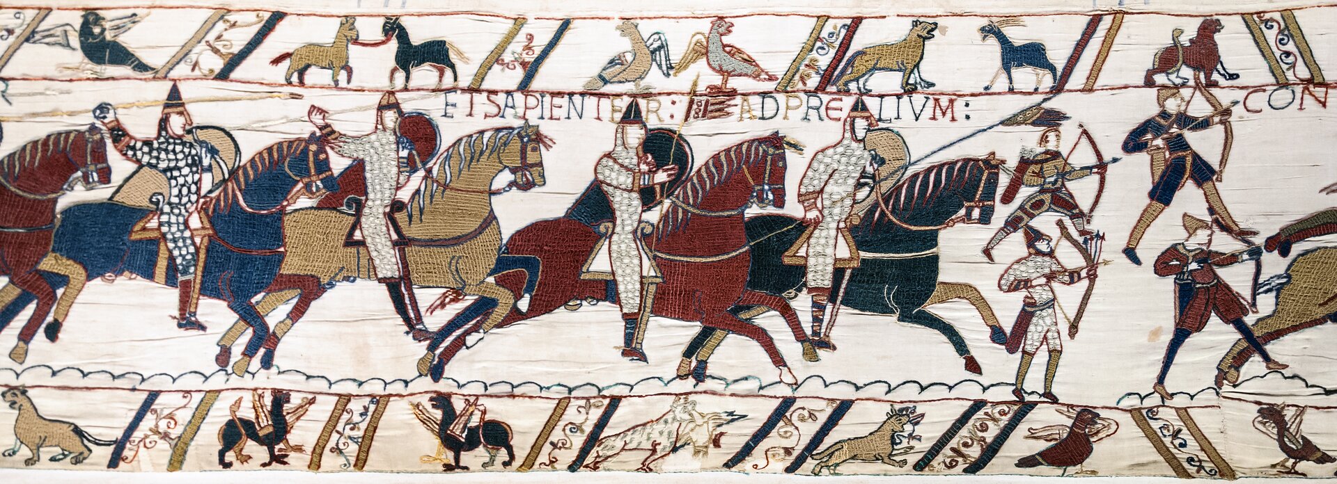 Ilustracja przedstawia fragment tkaniny z Bayeux. Ukazuje podbój Anglii przez Wilhelma Pierwszego Zdobywcę. Na ilustracji przedstawieni są rycerze na koniach. Po prawej stronie stoi czterech łuczników. Po lewej stronie konno jadą rycerze z podniesionymi rękoma. Nad nimi zamieszczony jest pas z symbolami zwierzęcymi oraz napis w języku łacińskim. Na dole ukazane są miniatury ze sceny walki.