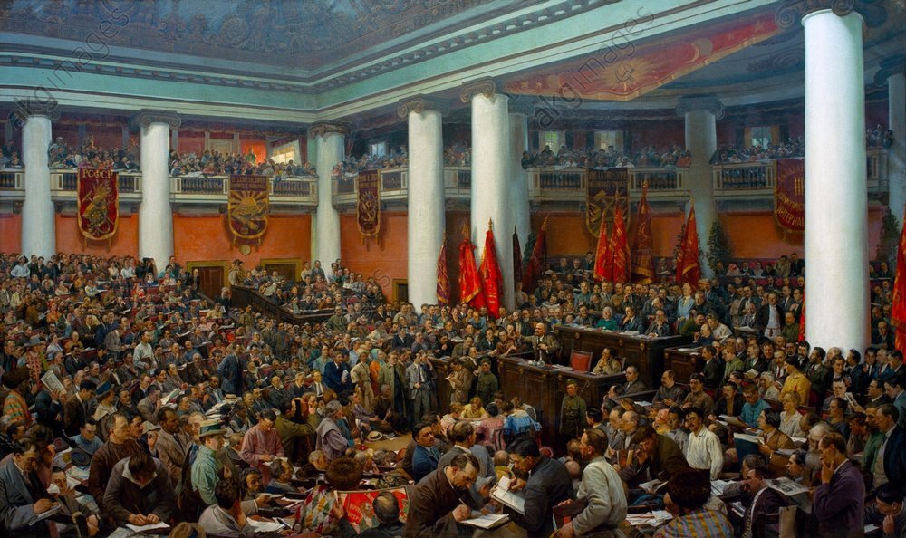 Ilustracja przedstawia przemówienie Lenina w radzieckim parlamencie. Większość ludzi słucha przemówienia, inni czytają gazety lub rozmawiają ze sobą. W sali widać kolumny podtrzymujące strop, flagi oraz zwisające z balkonu sztandary
