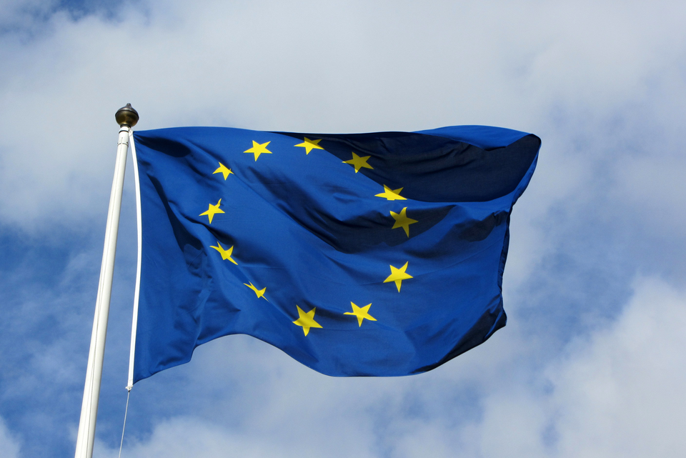 Zdjęcie przedstawia flagę Europy zawieszoną na maszcie. Maszt po lewej stronie zdjęcia. Flaga powiewa skierowana w prawo. Na granatowym tle 12 pięcioramiennych gwiazdek. Gwiazdy ułożone są w okrąg.