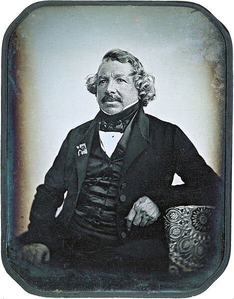 Portret Louisa Daguerre’a Jean-Baptiste Sabatier-Blot (1801–1881; czyt.: żą batist sabati-blo) – francuski malarz i dagerotypista. Źródło: Jean-Baptiste Sabatier-Blot, Portret Louisa Daguerre’a, 1844, dagerotypia, domena publiczna.