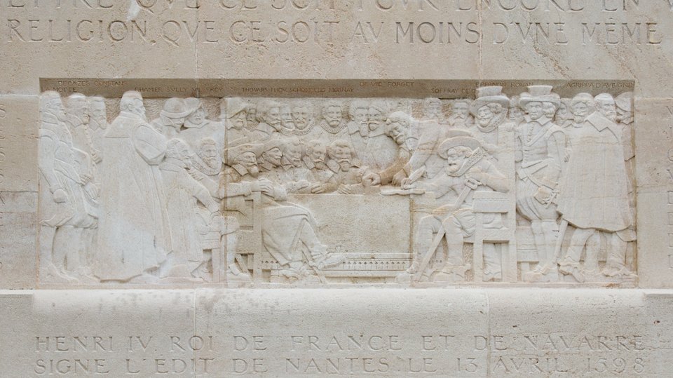 Relief na pomniku reformacji w Genewie przedstawiający podpisanie edyktu nantejskiego przez Henryka IV w 1598 r. Więcej o samym pomniku - por. informacje z lekcji 88. U dołu napis „HENRI IV ROI DE FRANCE ET DE NAVARRE SIGNE L’EDIT DE NANTES LE 13 AVRIL 1598” (Henryk IV król Francji i Nawarry podpisuje edykt Nantejski 13 kwietnia 1598). Relief na pomniku reformacji w Genewie przedstawiający podpisanie edyktu nantejskiego przez Henryka IV w 1598 r. Więcej o samym pomniku - por. informacje z lekcji 88. U dołu napis „HENRI IV ROI DE FRANCE ET DE NAVARRE SIGNE L’EDIT DE NANTES LE 13 AVRIL 1598” (Henryk IV król Francji i Nawarry podpisuje edykt Nantejski 13 kwietnia 1598). Źródło: Clément Bucco-Lechat, Wikimedia Commons, licencja: CC BY-SA 3.0.