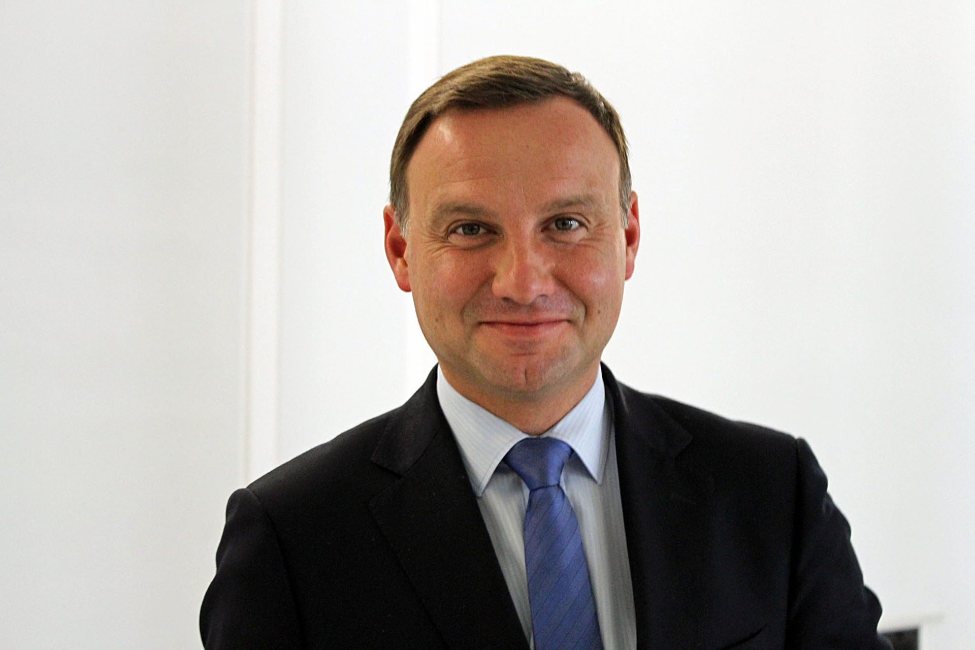 Kolorowe zdjęcie portretowe. Na zdjęciu mężczyzna w wieku około 45 lat. Zwrócony przodem do obserwatora. Twarz okrągła, z lekkim zarostem. Włosy ciemne, gładko zaczesane na bok. Czoło gładkie, wysokie. Oczy małe. Nos duży. Usta wąskie. Uszy przylegające. Ubrany w czarną marynarkę, błękitną koszulę. Niebieski krawat.