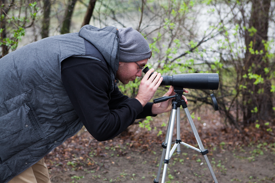 Fotografia człowieka patrzącego przez lunetę na statywie.