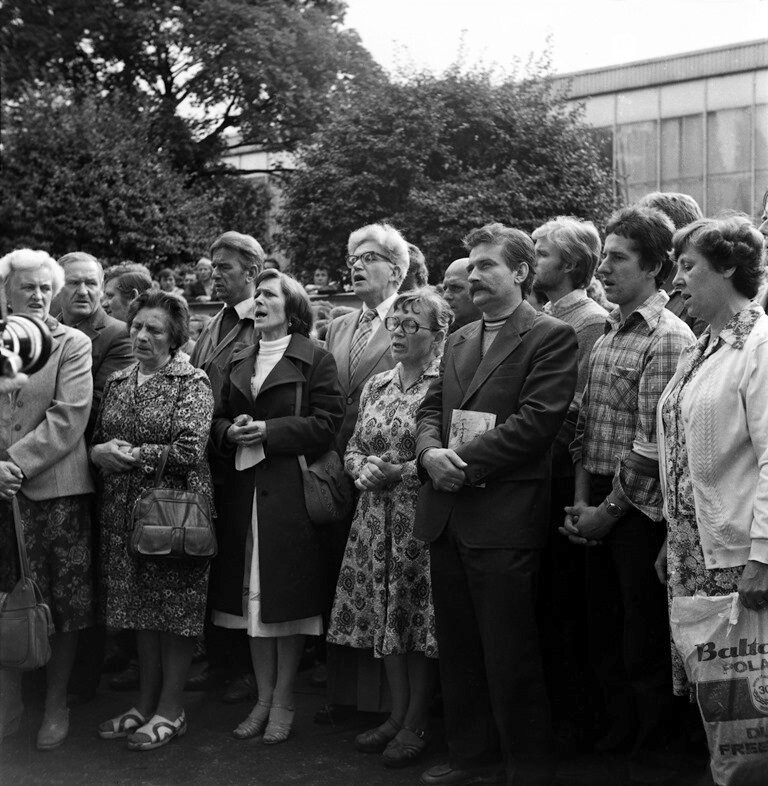 na zdjeciu grupa ludzi podczas mszy świętej na strajku w stoczni gdańskiej w 1980 r., wśrod nich Anna Walentynowicz i Lech Wałęsa
