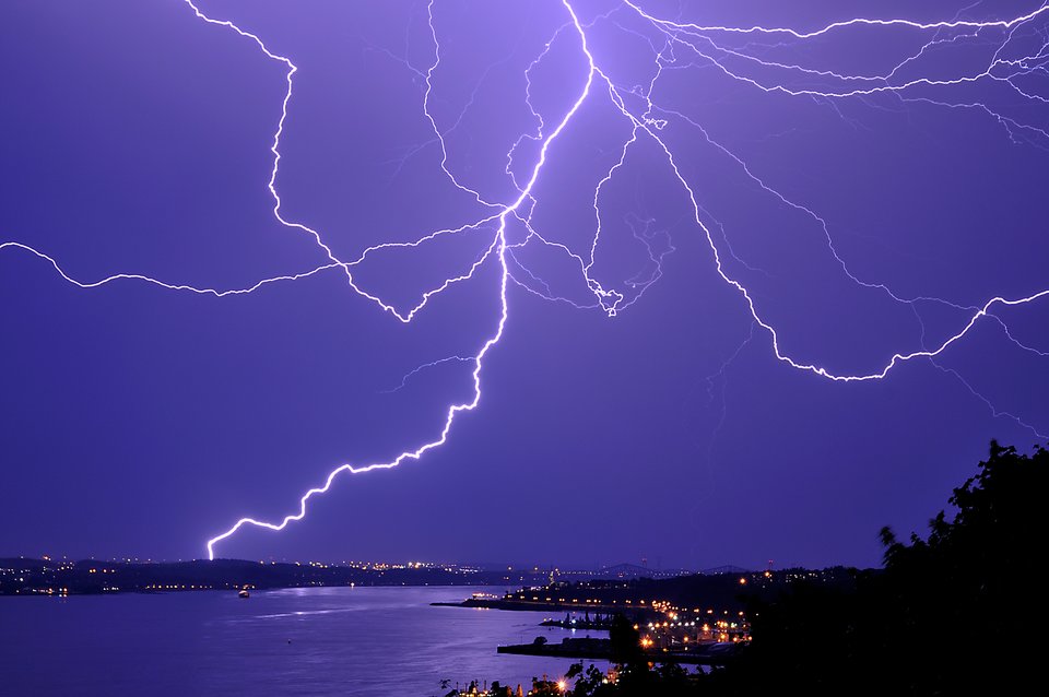 Na fotografii widoczne nocne bezchmurne niebo z rozbiegającymi się w różnych kierunkach białymi błyskawicami