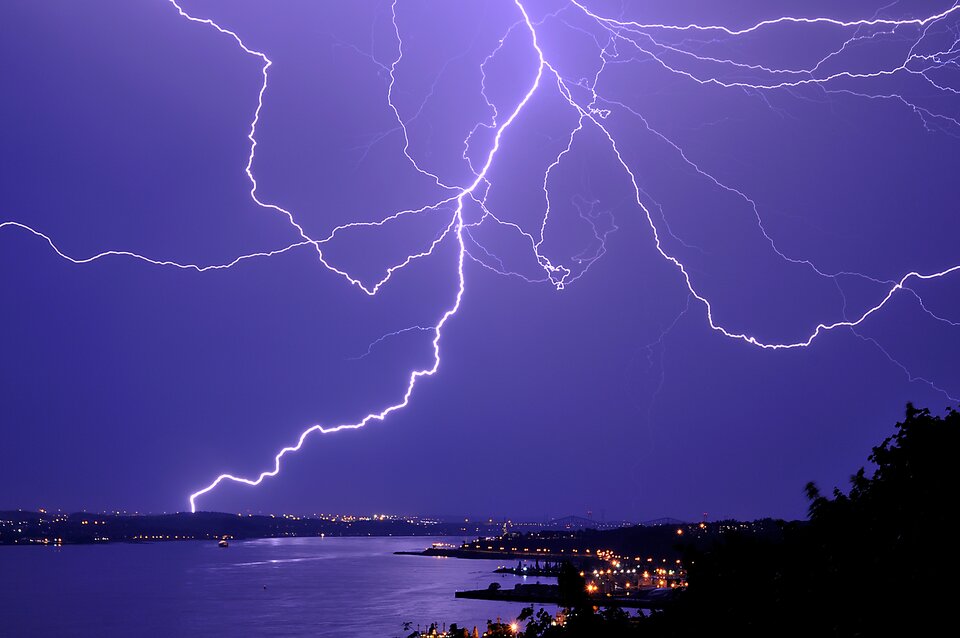 Na fotografii widoczne nocne bezchmurne niebo z rozbiegającymi się w różnych kierunkach białymi błyskawicami