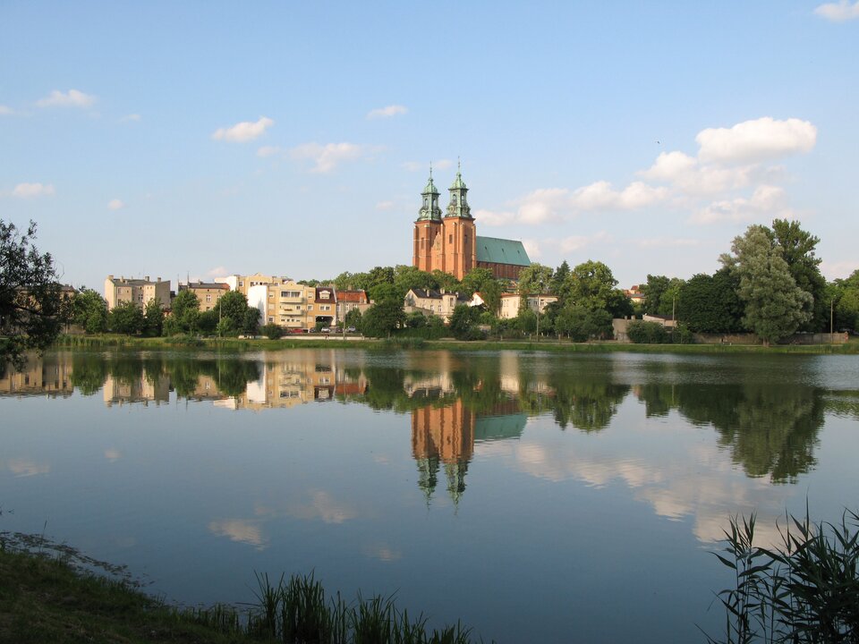 Na zdjęciu wysoki kościół z dwoma wieżami i zabudowa miejska nad brzegiem rzeki.