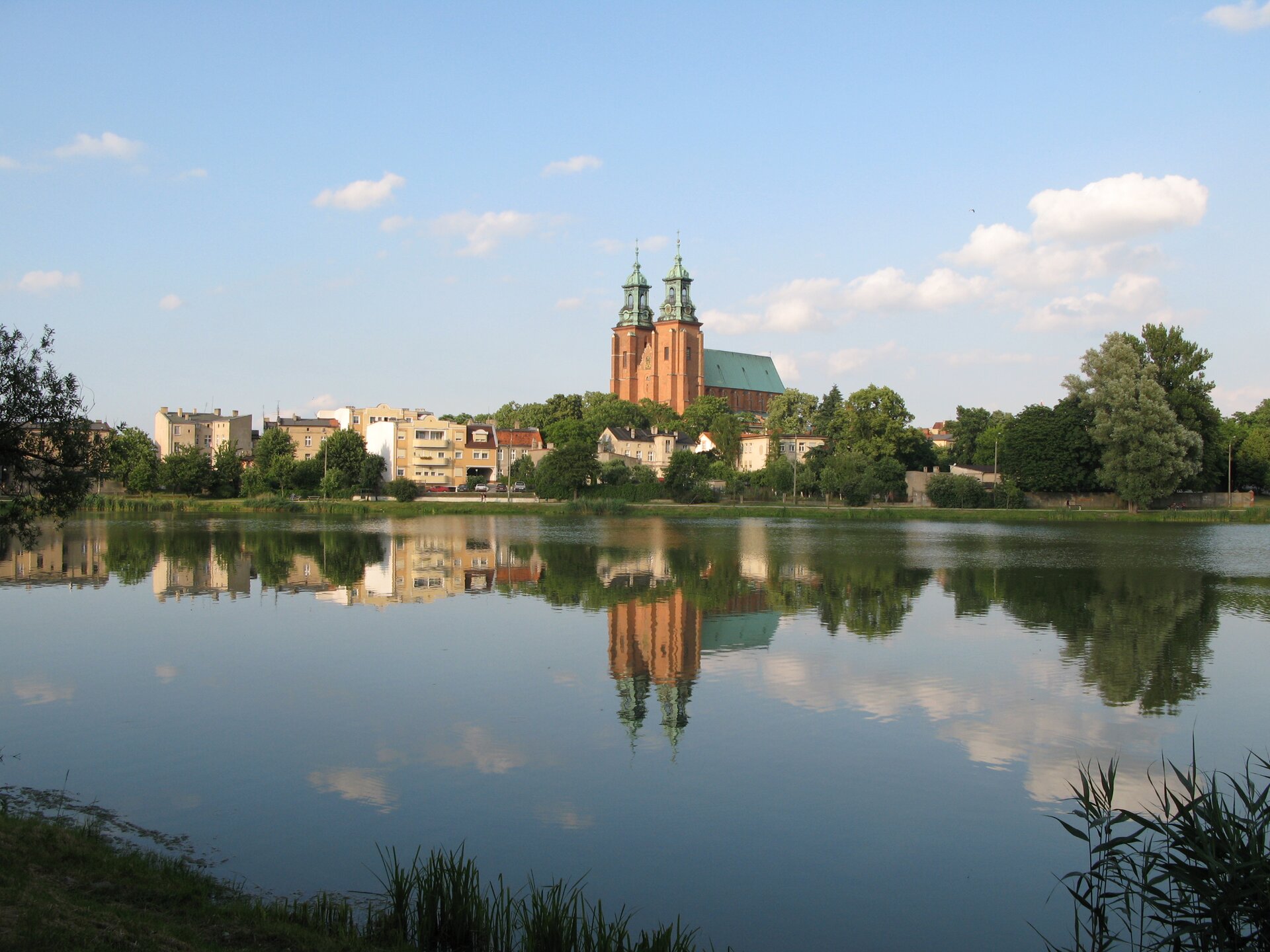 Na zdjęciu wysoki kościół z dwoma wieżami i zabudowa miejska nad brzegiem rzeki.