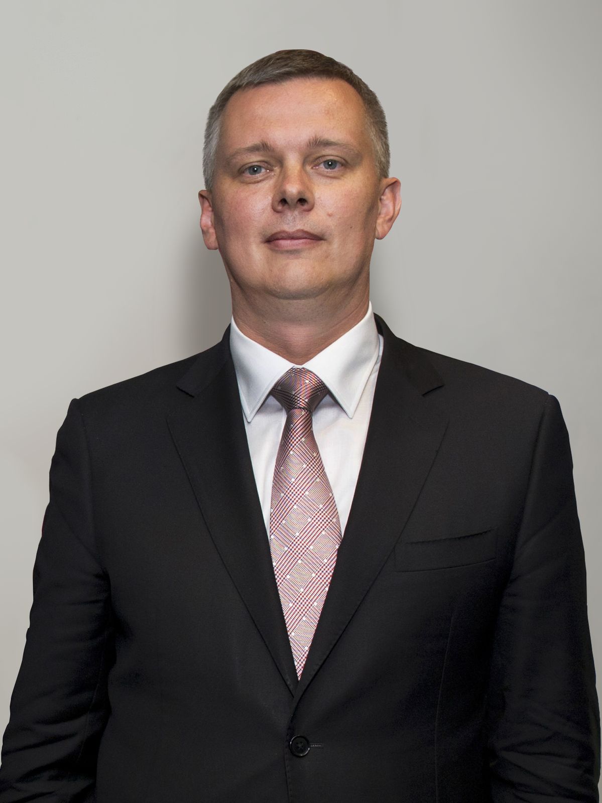 Zdjęcie portretowe Tomasza Siemioniaka. Mężczyzna w wieku około 50 lat, zwrócony przodem do odbiorcy. Włosy gładko zaczesane na bok. Siwe włosy na skroniach. Czoło wysokie, gładkie. Brwi jasne, oczy małe. Nos duży, zadarty. Usta pełne. Twarz pociągła, gładko ogolona. Uszy przylegające. Ubrany w czarny garnitur, białą koszulę. Różowy krawat we wzorki.