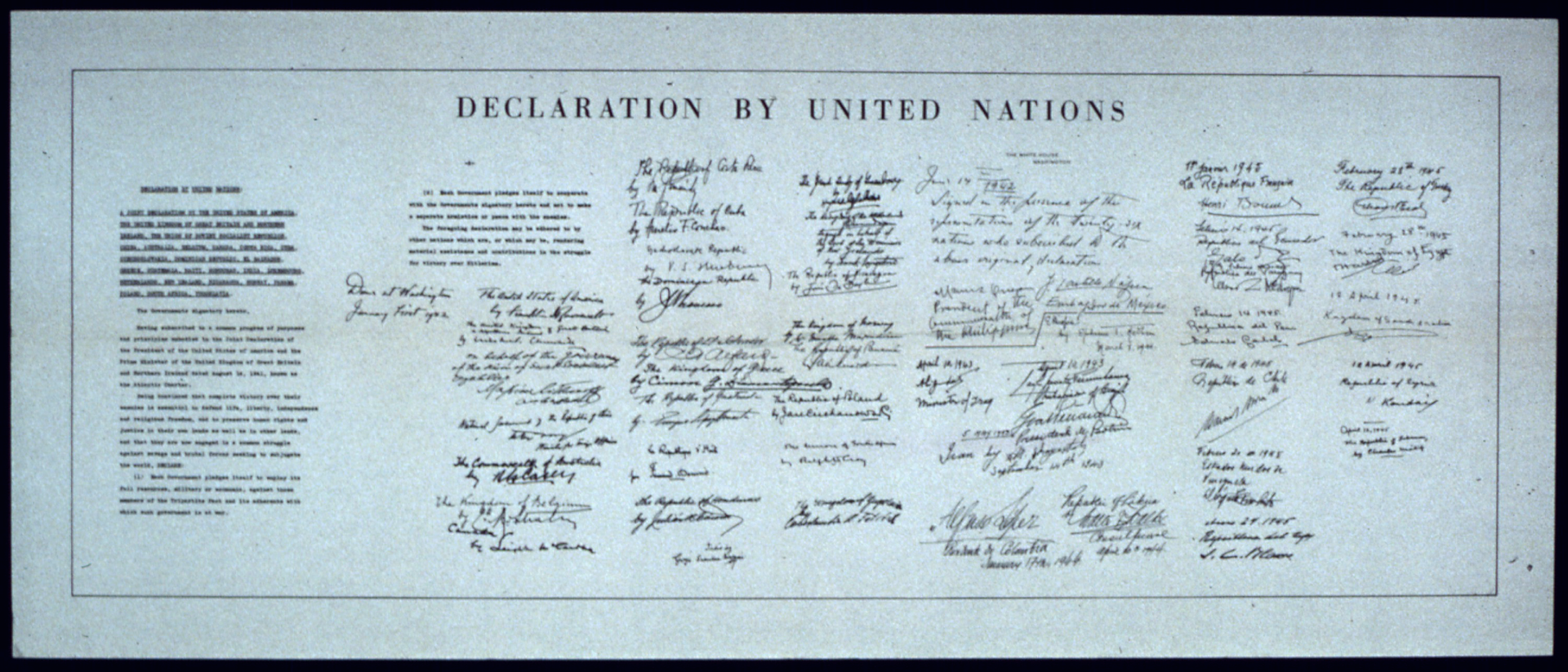 Ilustracja przedstawia duży papierowy dokument. To biało-czarne zdjęcie karty Narodów Zjednoczonych. Na górze dokumenty poziomy napis w języku angielskim: declaration by United Nations. Po lewej stronie treść deklaracji w dwóch kolumnach. Na prawo od treści 26 podpisów wykonanych przez przedstawicieli państw członków założycieli. Podpisy ułożone są w 7 kolumnach. Kolumny jedna obok drugiej.