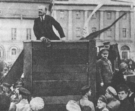 Lenin przemawiający na placu Czerwonym. Po prawej stronie, oparty o trybunę stoi Lew Trocki Lenin przemawiający na placu Czerwonym. Po prawej stronie, oparty o trybunę stoi Lew Trocki Źródło: domena publiczna.
