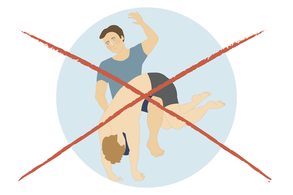 Ilustracja w kształcie koła. Mężczyzna klęczy na lewym kolanie. Na prawym leży osoba poszkodowana. Osoba poszkodowana jest „przewieszona” przez kolano mężczyzny. Głowa poszkodowanego zwieszona w dół. Ręce wyprostowane zwisają w dół wspierając się na podłożu. Klęczący mężczyzna lewą ręką przytrzymuje poszkodowanego. Prawa ręka uniesiona w górę, zgięta w łokciu. Cała ilustracja przekreślona dwoma skrzyżowanymi czerwonymi liniami.