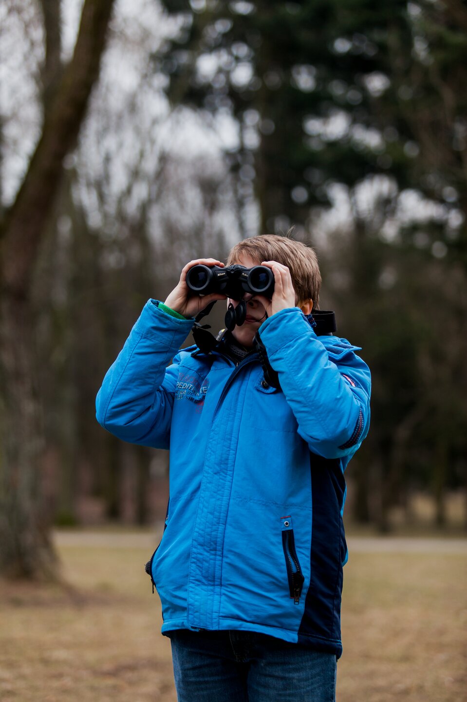 Fotografia młodego człowieka w terenie patrzącego przez lornetkę.