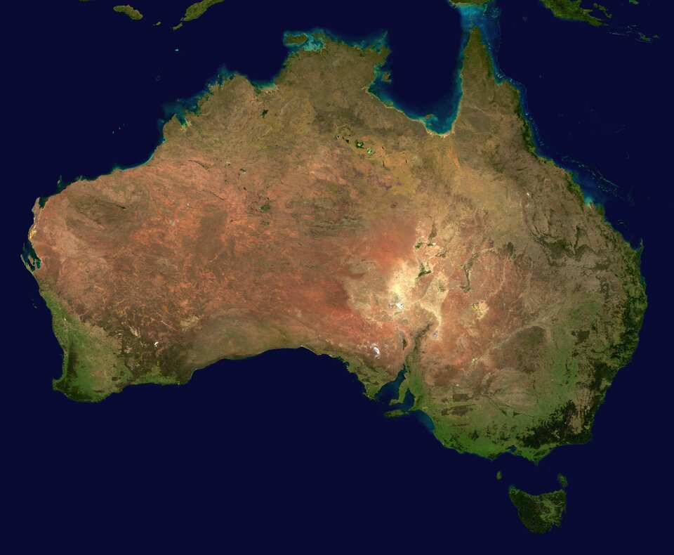 Na zdjęciu satelitarnym kontynent Australii, widoczne tereny zielone nad brzegiem morza i brunatne oraz żółte wewnątrz kontynentu. Rozczłonkowana linia brzegowa na wschodzie kontynentu.