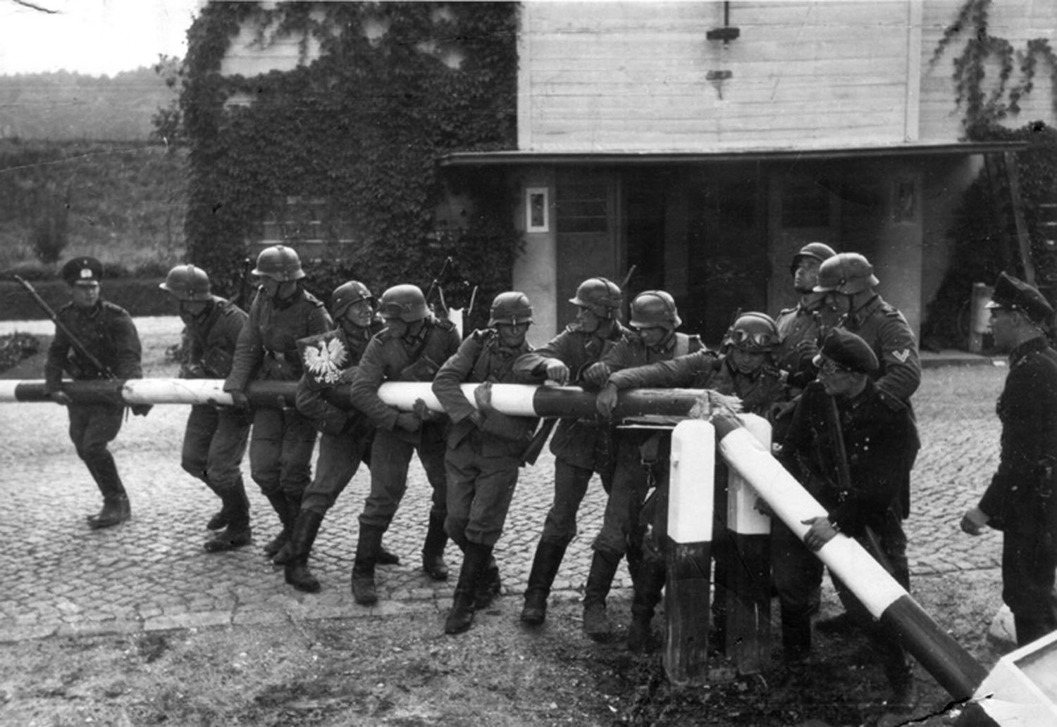 Zdjęcie ukazujące Niemców wyłamujących szlaban na przejściu granicznym w Sopocie, dnia 1 IX 1939 r. (zdjęcie wykonano na potrzeby propagandy 14 IX , w rzeczywistości 1 IX trwały tam ciężkie walki) Zdjęcie ukazujące Niemców wyłamujących szlaban na przejściu granicznym w Sopocie, dnia 1 IX 1939 r. (zdjęcie wykonano na potrzeby propagandy 14 IX , w rzeczywistości 1 IX trwały tam ciężkie walki) Źródło: domena publiczna.