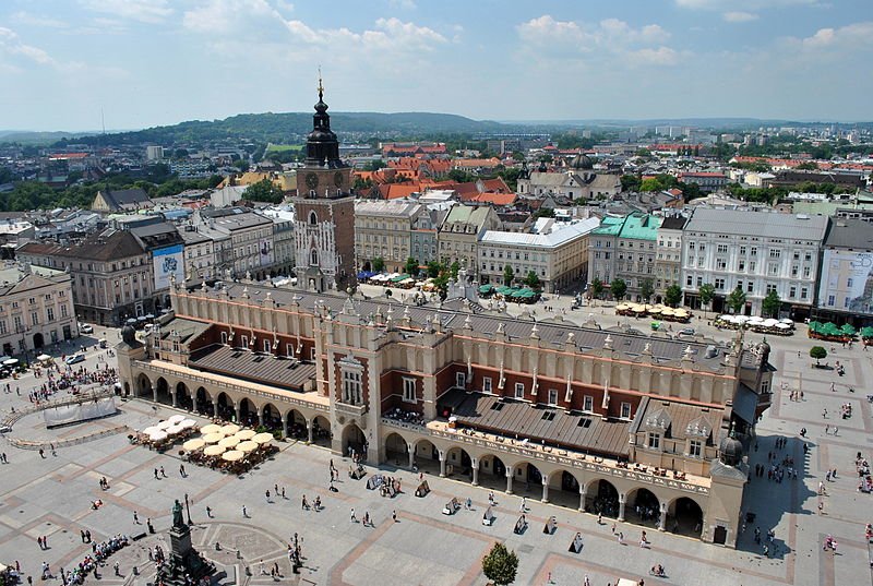 Na fotografii widać dwa budynki stojące na środku krakowskiego rynku – Sukiennice i wystającą zza nich wieżę ratusza Na fotografii widać dwa budynki stojące na środku krakowskiego rynku – Sukiennice i wystającą zza nich wieżę ratusza Źródło: Maatex, Wikimedia Commons, licencja: CC BY-SA 3.0.