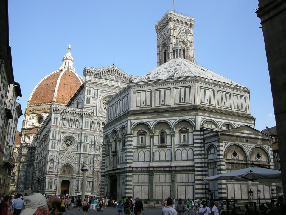 Florencja – katedra – widok ogólny z baptysterium na pierwszym planie, dzwonnicą, a w tle katedrą i kopułą. Katedrę pw. Santa Maria del Fiore (Świętej Marii Kwietnej) zaczęto wznosić w 1296 r. i budowa jej trwa nieprzerwanie do dnia dzisiejszego. Główny korpus nawy głównej ukończono w XIV w. (1295-1379 r. – szerokość 38 m, długość 153 m); kopułę w stanie surowym wzniesiono w latach 1418-1443 (wysokość 107 m, średnica kopuły 45 m); stojącą obok dzwonnicę rozpoczęto budować w 1298 r., a jej dach zwieńczono w 1359 r. (wysokość 85 m). Fasadę rozpoczęto w XIII w., ale w 1588 r. rozebrano ją jako „niemodną" i rozpoczęto jej realizację od nowa. Ostatnie prace przy fasadzie miały miejsce w XIX w.; obecnie trwają prace przy wykończeniu kopuły. Na zdjęciu widać m.in. fragment ukończonej w XIX w. fasady głównej; przy kopule nad okrągłym oknem (nazywanym „okulusem”) widać fragment ciągle jeszcze nie skończonego gzymsu wieńczącego. Florencja – katedra – widok ogólny z baptysterium na pierwszym planie, dzwonnicą, a w tle katedrą i kopułą. Katedrę pw. Santa Maria del Fiore (Świętej Marii Kwietnej) zaczęto wznosić w 1296 r. i budowa jej trwa nieprzerwanie do dnia dzisiejszego. Główny korpus nawy głównej ukończono w XIV w. (1295-1379 r. – szerokość 38 m, długość 153 m); kopułę w stanie surowym wzniesiono w latach 1418-1443 (wysokość 107 m, średnica kopuły 45 m); stojącą obok dzwonnicę rozpoczęto budować w 1298 r., a jej dach zwieńczono w 1359 r. (wysokość 85 m). Fasadę rozpoczęto w XIII w., ale w 1588 r. rozebrano ją jako „niemodną" i rozpoczęto jej realizację od nowa. Ostatnie prace przy fasadzie miały miejsce w XIX w.; obecnie trwają prace przy wykończeniu kopuły. Na zdjęciu widać m.in. fragment ukończonej w XIX w. fasady głównej; przy kopule nad okrągłym oknem (nazywanym „okulusem”) widać fragment ciągle jeszcze nie skończonego gzymsu wieńczącego. Źródło: Sailko, Wikimedia Commons, licencja: CC BY-SA 3.0.