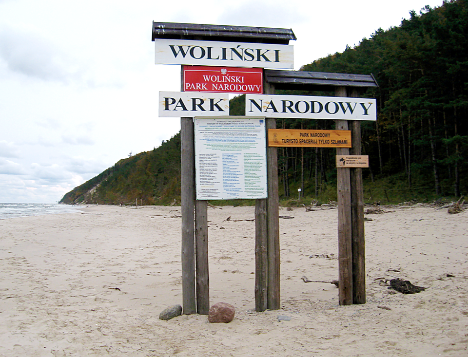 Fotografia prezentuje tablice informacyjne umieszczone na palach znajdujących się na plaży nadmorskiej