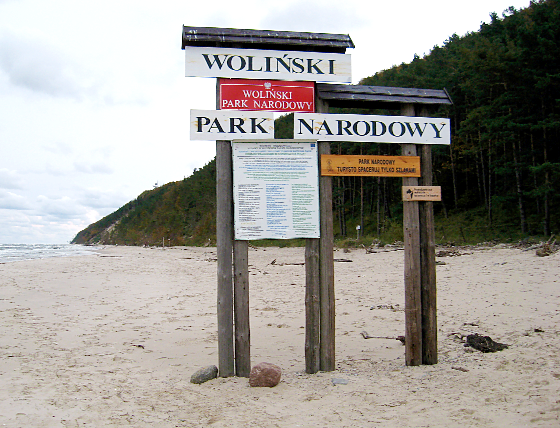 Fotografia prezentuje tablice informacyjne umieszczone na palach znajdujących się na plaży nadmorskiej
