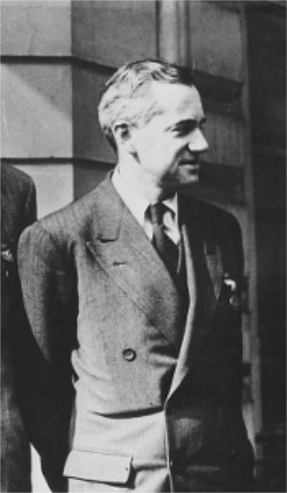 Zdjęcie przedstawia Otto Firscha. Fotografia czarno-biała. Na zdjęciu mężczyzna w wieku ok. 45 lat, szczupły. Zwrócony w bok, widoczny prawy profil. Czoło wysokie, włosy siwiejące. Nos duży. Mężczyzna delikatnie się uśmiecha. Uszy proporcjonalne, przylegające. Mężczyzna jest ubrany w trzyczęściowy garnitur w prążki, białą koszulę oraz ciemny krawat.