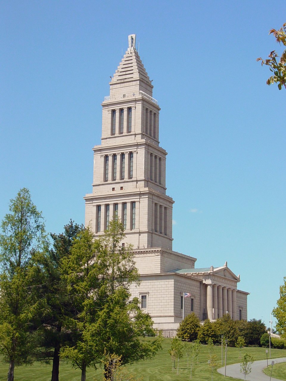 George Washington Masonic National Memorial – Narodowy Pomnik Wolnomularski poświęcony Jerzemu Waszyngtonowi w Alexsandrii w stanie Wirginia nieopodal stołecznego Waszyngtonu. Pomnik powstał w latach 1823-1932. Prezentowany budynek główny ma wiele znaczeń i nawiązań symbolicznych – np. portyk wejściowy przypomina Partenon, kolejne kondygnacje zbudowane zostały wg kolejnych porządków greckich: doryckiego, jońskiego, korynckiego, całość zwieńczono czymś, co przypomina piramidę, a jednocześnie jest nawiązaniem do latarni morskiej stojącej w porcie Aleksandrii na wyspie Faros (jeden z cudów świata antycznego). Jedno z pięter stanowi muzeum poświęcone Jerzemu Waszyngtonowi, który też był członkiem loży masońskiej. George Washington Masonic National Memorial – Narodowy Pomnik Wolnomularski poświęcony Jerzemu Waszyngtonowi w Alexsandrii w stanie Wirginia nieopodal stołecznego Waszyngtonu. Pomnik powstał w latach 1823-1932. Prezentowany budynek główny ma wiele znaczeń i nawiązań symbolicznych – np. portyk wejściowy przypomina Partenon, kolejne kondygnacje zbudowane zostały wg kolejnych porządków greckich: doryckiego, jońskiego, korynckiego, całość zwieńczono czymś, co przypomina piramidę, a jednocześnie jest nawiązaniem do latarni morskiej stojącej w porcie Aleksandrii na wyspie Faros (jeden z cudów świata antycznego). Jedno z pięter stanowi muzeum poświęcone Jerzemu Waszyngtonowi, który też był członkiem loży masońskiej. Źródło: Ben Schumin, Wikimedia Commons, licencja: CC BY-SA 2.5.