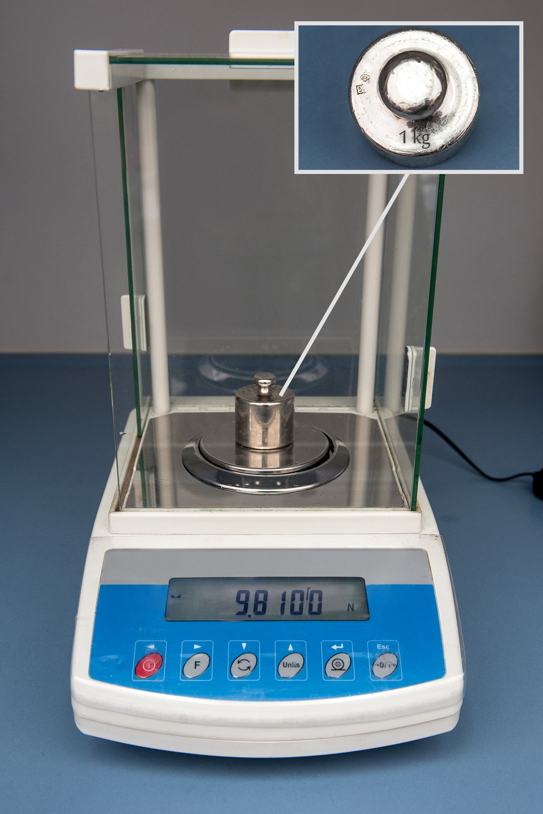 Fotografia wagi elektronicznej ustawionej na wyświetlanie wskazań w niutonach. Na szalce odważnik o masie 1 kg. Wyraźnie widać wyświetlacz wagi elektronicznej. Na wyświetlaczu widać wyraźnie wartość oraz jednostkę (N). Wyświetlana wartość to 9,81 N.