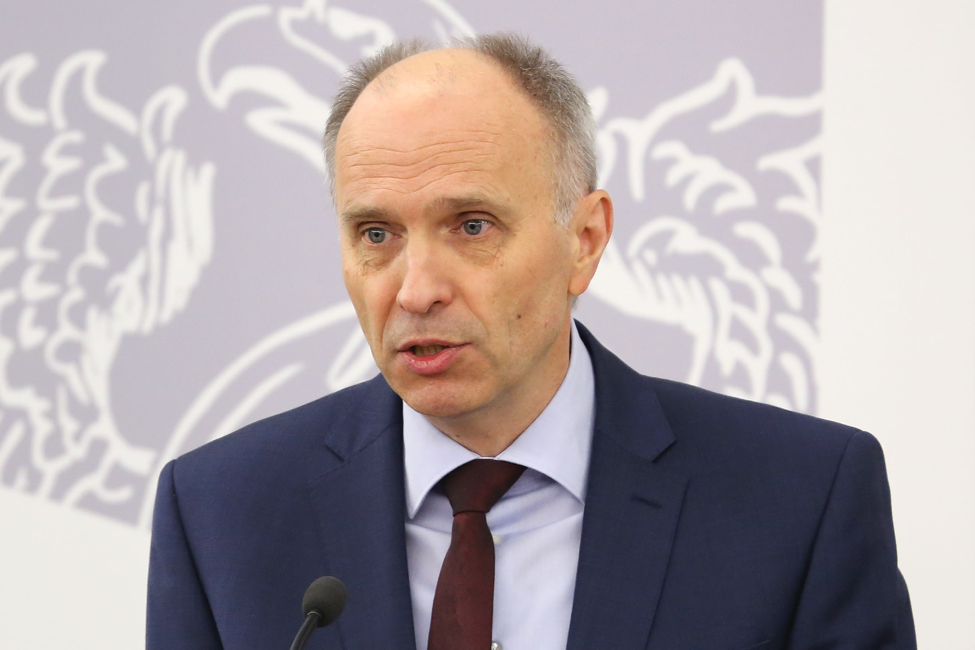 Kolorowe zdjęcie portretowe Andrzeja Jakubiaka. Mężczyzna w wieku około 55 lat przodem zwrócony do obserwatora zdjęcia. Włosy siwe z oznakami łysienia na górze głowy. Czoło wysokie, pokryte poziomymi zmarszczkami. Brwi jasne, wąskie. Oczy małe. Nos duży, szeroki na końcu. Usta wąskie. Twarz pociągła, z lekkim zarostem. Uszy duże, przylegające. Mężczyzna ubrany w granatową marynarkę, błękitną koszulę i ciemny bordowy krawat.