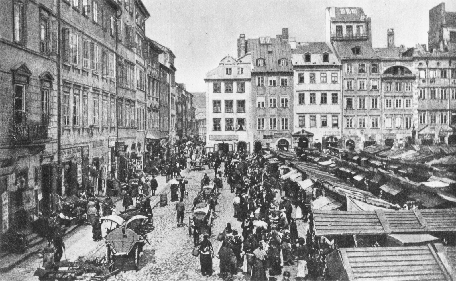 Ilustracja przedstawia rynek Starego Miasta w Warszawie. Jest to kwadratowy plac otoczony kamieniczkami. Na środku placu znajdują się liczne drobne stragany. Po rynku spaceruje bardzo dużo ludzi, jeżdżą również furmanki zaprzężone w konie.