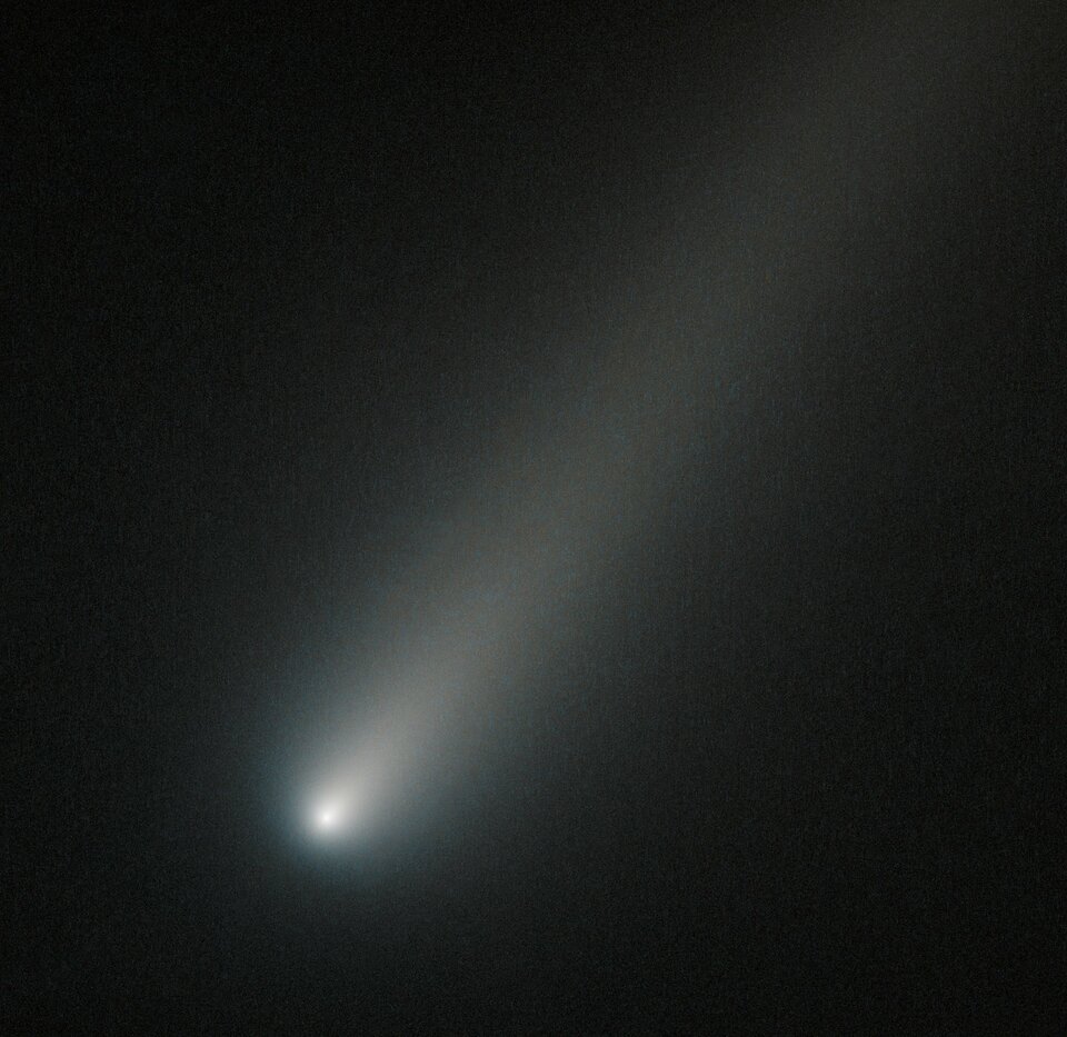 Zdjęcie przedstawia kometę ISON uwiecznioną przez teleskop Hubble'a podczas przelotu przez orbitę Marsa podczas zbliżenia do Układu Słonecznego w 2013 roku na miesiąc przed osiągnięciem peryhelium. Kometa zajmuje praktycznie cały kadr, jej jądro świeci jasnym światłem, a ogon jest wyraźny.