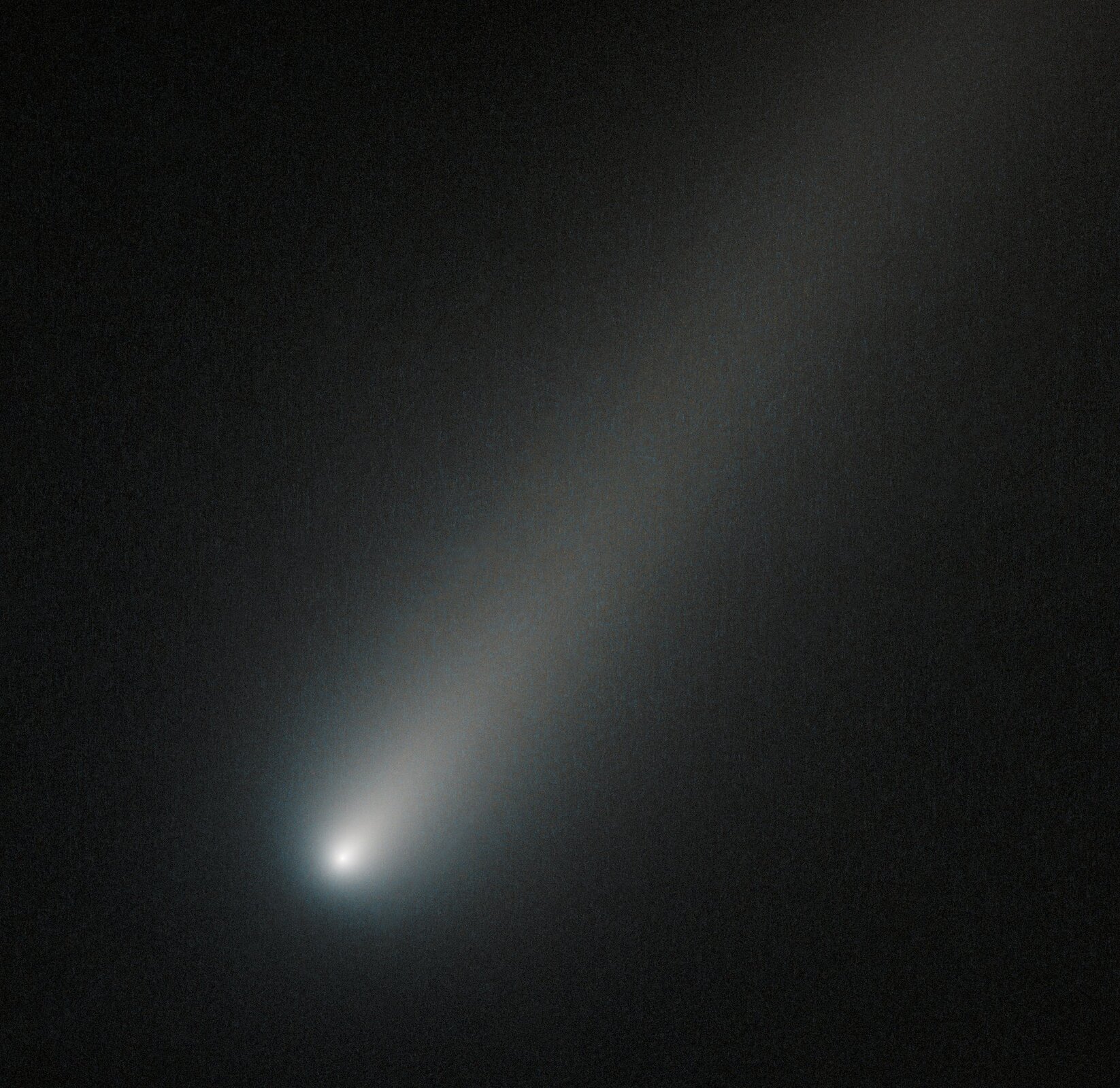 Zdjęcie przedstawia kometę ISON uwiecznioną przez teleskop Hubble'a podczas przelotu przez orbitę Marsa podczas zbliżenia do Układu Słonecznego w 2013 roku na miesiąc przed osiągnięciem peryhelium. Kometa zajmuje praktycznie cały kadr, jej jądro świeci jasnym światłem, a ogon jest wyraźny.