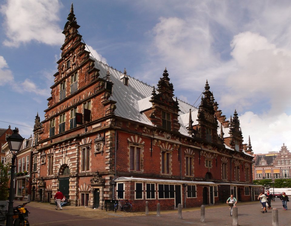 Haarlem – hala targowa (ławy rzeźnicze – jatki) – wybudowana na wielkim Rynku w Haarlemie w latach 1602-1603. Jest to północna odmiana architektury renesansowej. Zwróć uwagę na materiał, jakim się posłużono do budowy ścian i detalu wykończeniowego; potem na okna, ich akcentowanie, kształt oraz rozmieszczenie, wreszcie na szczyt budynku i jego ozdoby. Haarlem – hala targowa (ławy rzeźnicze – jatki) – wybudowana na wielkim Rynku w Haarlemie w latach 1602-1603. Jest to północna odmiana architektury renesansowej. Zwróć uwagę na materiał, jakim się posłużono do budowy ścian i detalu wykończeniowego; potem na okna, ich akcentowanie, kształt oraz rozmieszczenie, wreszcie na szczyt budynku i jego ozdoby. Źródło: Welleschik, Wikimedia Commons, licencja: CC BY-SA 3.0.