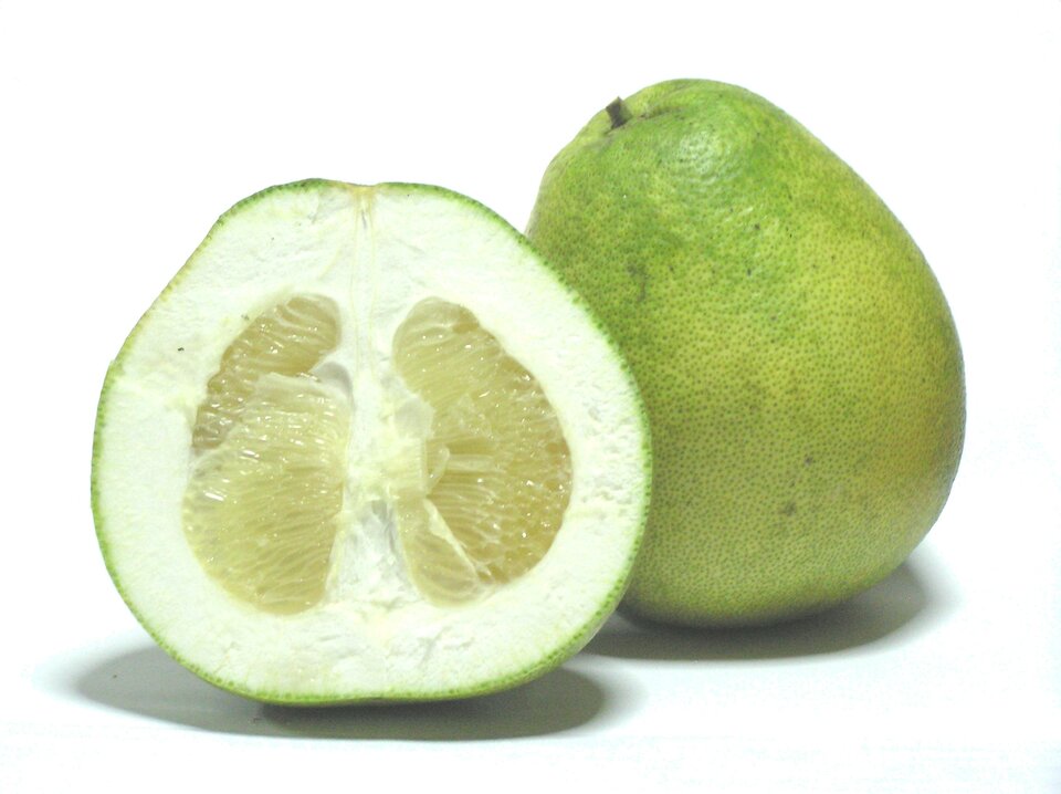 Fotografia przedstawia dwa jasnozielone owoce pomelo. Jeden z nich jest przekrojony pionowo dla uwidocznienia miąższu.