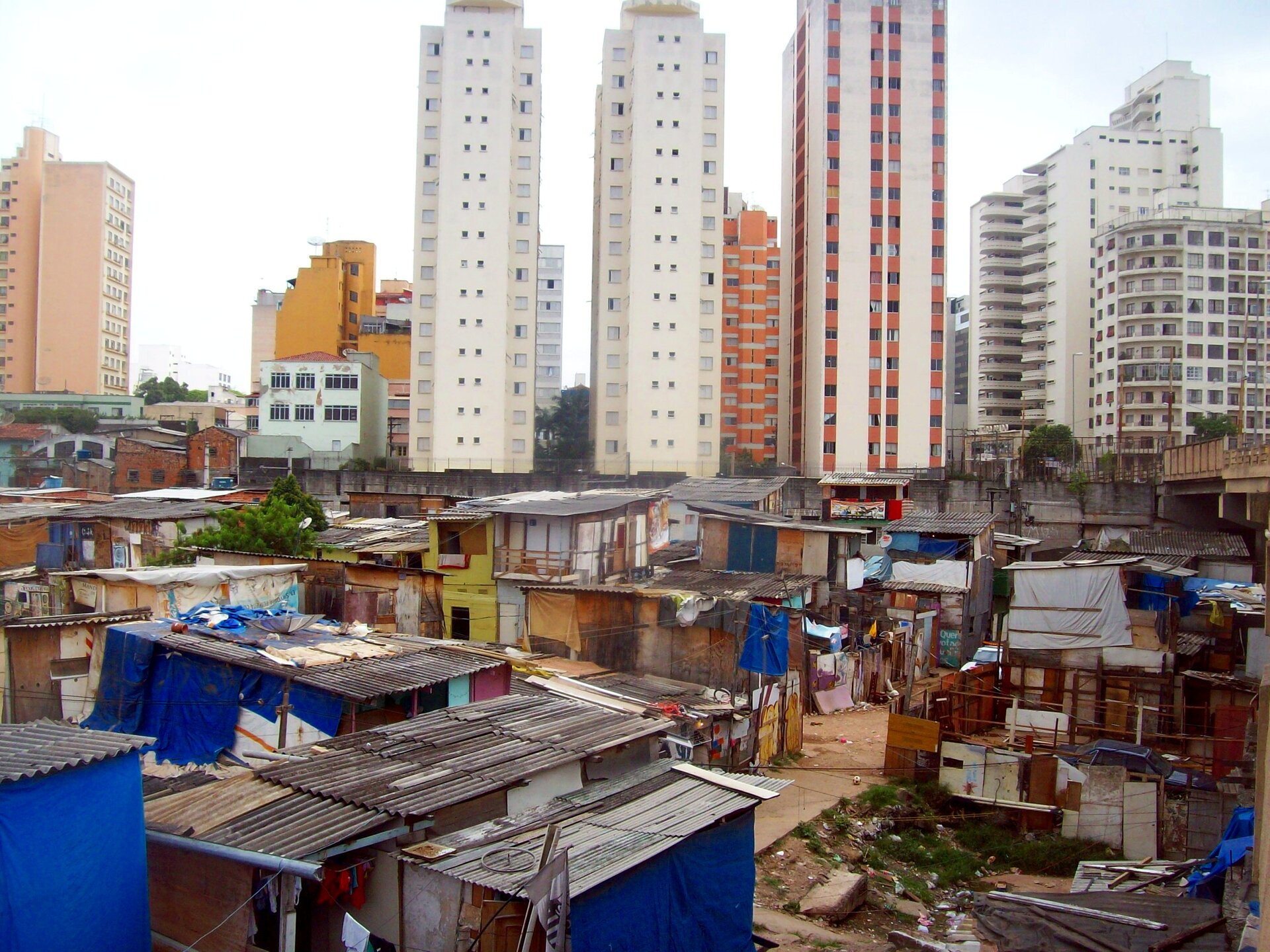 Na zdjęciu dzielnica mieszkaniowa w Sao Paulo. Na pierwszym planie favela z prowizorycznymi domami. Domy zbudowane z najtańszych materiałów: tektury, dykty, blachy, desek. W tle wieżowce.