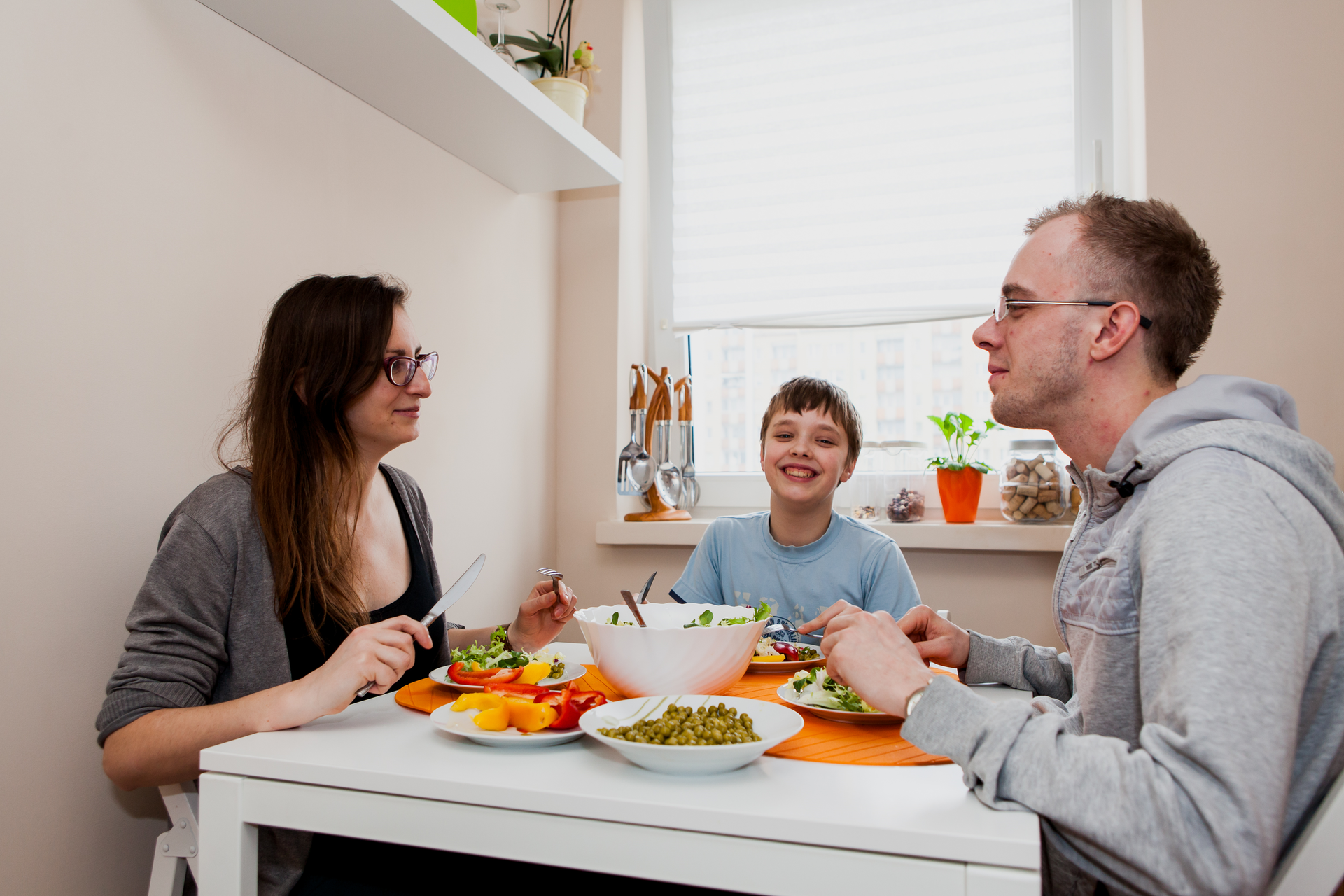 Fotografia przedstawiająca radosną rodzinę jedzącą zdrowy posiłek, pełen warzyw i owoców, bez produktów smażonych, pełnych tłuszczu.