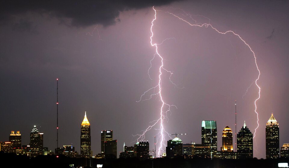 Fotografia przedstawia miasto nocą podczas burzy. Na fotografii ujęto moment uderzenia pioruna, któremu towarzyszy zjawisko świetlne o nierównomiernym kształcie. Podczas burz nie wolno chować się przed deszczem pod drzewami i innymi wysokimi przedmiotami.