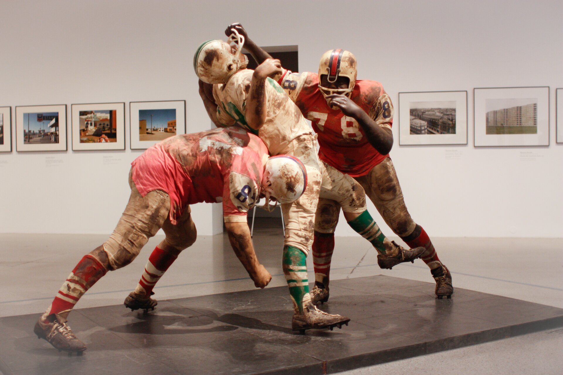 Ilustracja przedstawia pracę Duane Hensona „Football Vignette”. Rzeźba ta przedstawia scenę walki o piłkę. Rzeźba składa się z trzech postaci - dwóch w czerwonym stroju i jedna postać w białym.