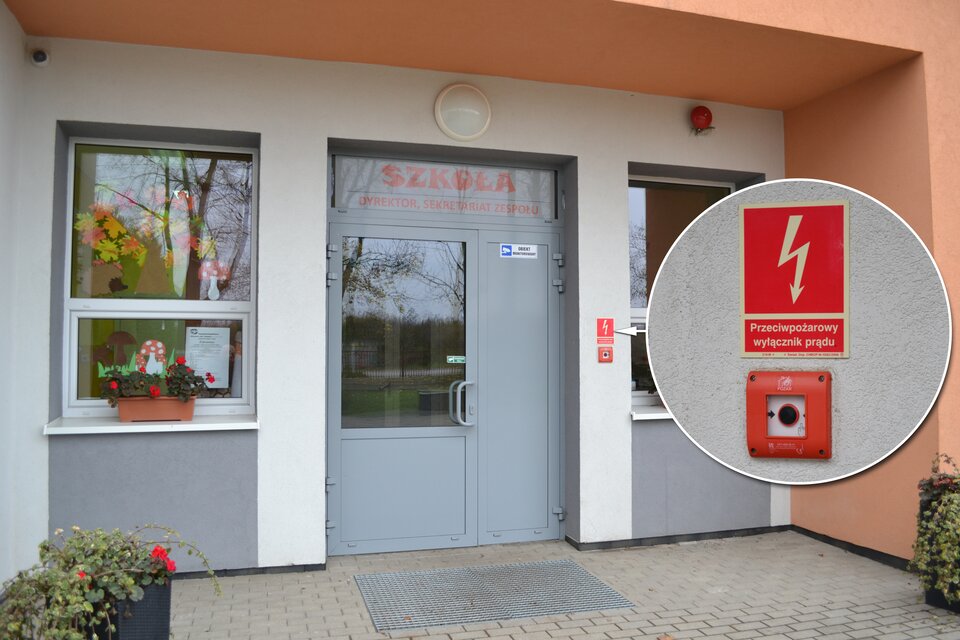 Kolorowe ujęcie głównego wejścia do budynku szkoły za dnia. Wejście to duże przeszklone pojedyncze drzwi z czerwonym napisem szkoła powyżej. Z prawej strony drzwi mieście się przeciwpożarowy wyłącznik prądu, który sygnalizuje czerwona ramka. Powyżej czerwona prostokątna tabliczka. Tabliczka podzielona na dwie części. Górna część, zajmująca dwie trzecie tabliczki, to czerwony prostokąt. Przez środek prostokąta przebiega biała błyskawica w kształcie strzałki z grotem skierowanym ku dołowi. W połowie strzałka jest zakrzywiona w formie zygzaka. Dół tabliczki to biały napis: główny wyłącznik prądu.